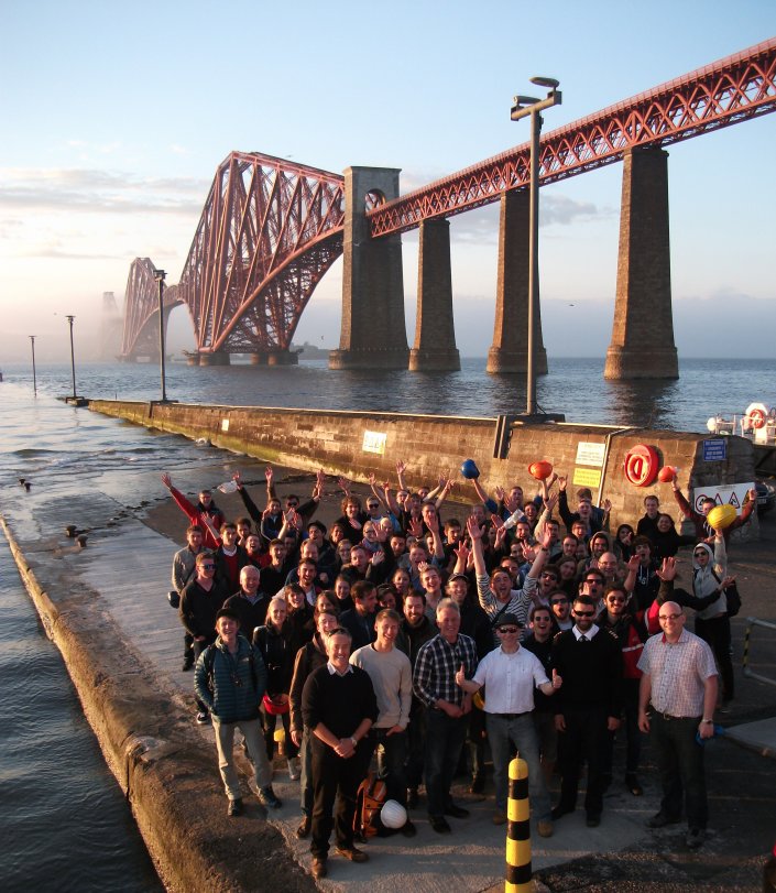 Eine Gruppe aus Studierenden und Professoren staht vor der Forth Bridge in dern Nähe von Edinburgh