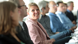 Teilnehmer eines Seminars sitzen in einer Reihe, eine Teilnehmerin lächelt ihrem Nachbarn zu (Bild: Thilo Schmülgen/FH Köln)