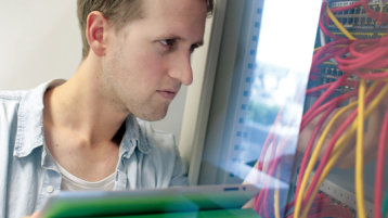Ein Student der Fakultät für Informations-, Medien- und Elektrotechnik mit IPad vor Kabeln (Bild: Thilo Schmülgen/FH Köln)
