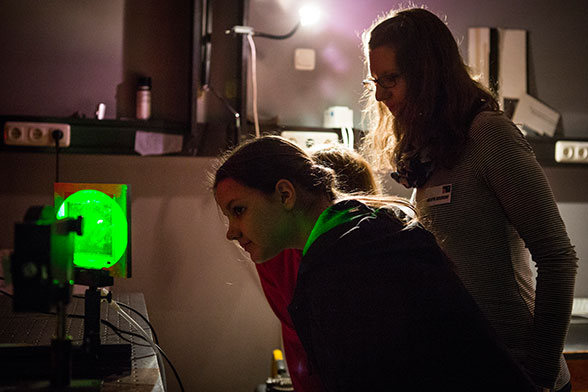 Drei Mädchen betrachten ein mit grünem Laser angeleuchtetes Hologramm.