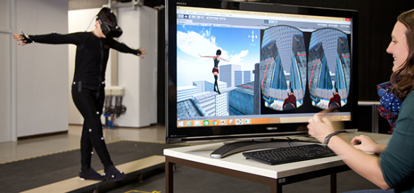 Eine Frau in VR-Montur balanciert auf einer Planke. Eine andere Frau betrachtet auf einem Monitor die Avatar Ansicht und Subjektive.