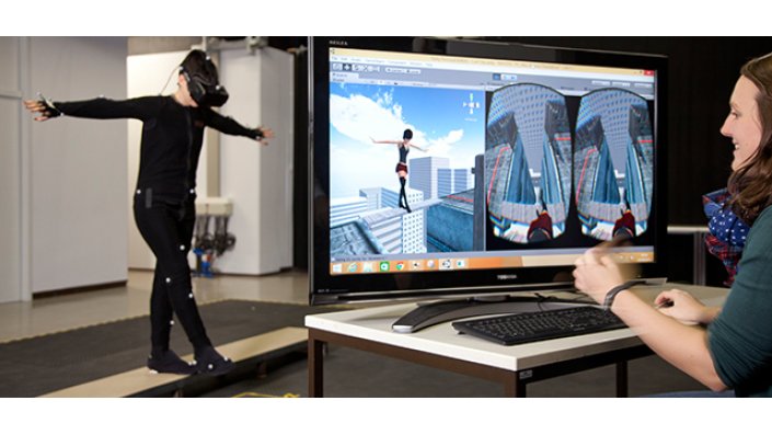 Eine Frau in VR-Montur balanciert auf einer Planke. Eine andere Frau betrachtet auf einem Monitor die Avatar Ansicht und Subjektive.