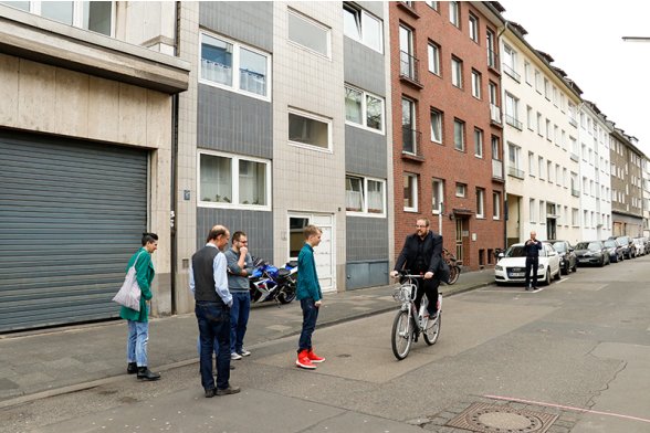 Ein Mann fährt Fahrrad, mehrere Personen schauen ihm dabei zu.