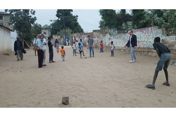 Erwachsene und Kinder spielen Fußball auf einer Sandpiste.