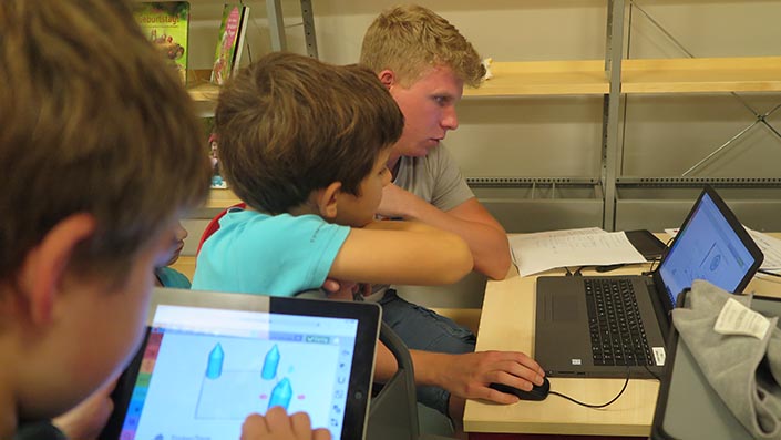 Zwei Kinder und ein Student der Projektgruppe arbeiten an einem Tabletcomputer und an einem Notebook
