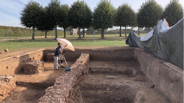 Zur Dokumentation werden die Grabungsprozesse fotografiert, je nach Sonnenstand helfen Schirm und Planen für eine gleichmäßige Ausleuchtung.