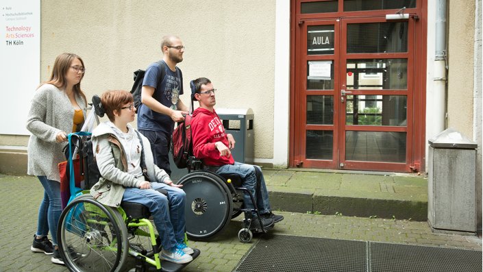 Zwei Personen im Rollstuhl werden an der Aula vorbeigeschoben