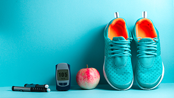 Insulinspritzen, ein Blutzuckermessgerät, ein Apfel und Sportschuhe (Bild: AdobeStock/Goffkein)
