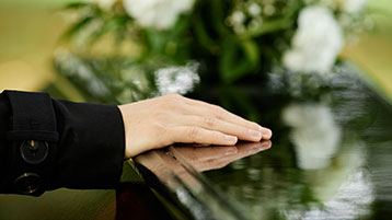 Eine Hand liegt auf einem schwarzen Sargdeckel. (Bild: AdobeStock/Seventyfour)