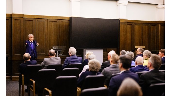 Publikum im Hörsaal, vorne steht Theologe und Kabarettist Pfarrer Rainer Schmidt