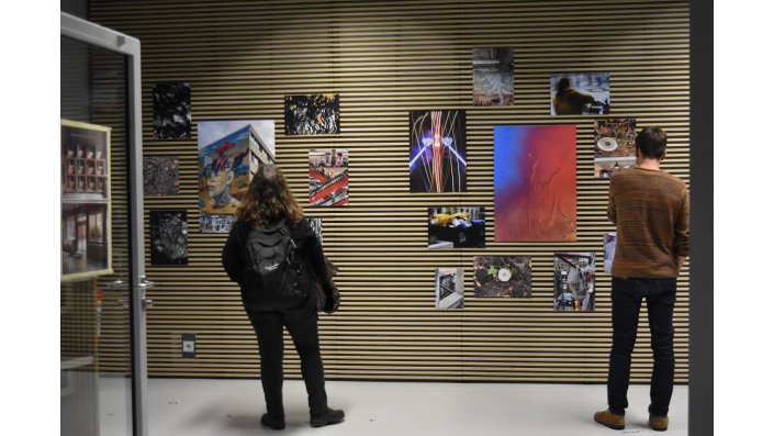 zwei Personen in Rückenansicht vor einer Wand mit Fotografien