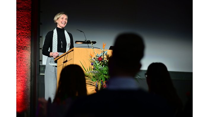 Prof. Dr. Sylvia Heuchemer, steht auf einer Bühne an einem Rednerpult und begrüßt die Teilnehmer*innen des diesjährigen Meet and Greet.