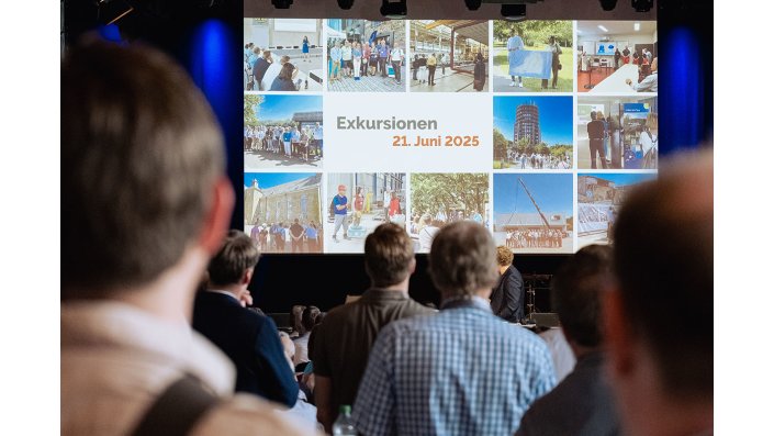 Personen schauen auf eine Präsentationsprojektion auf der "Exkursionen 21. Juni 2025" geschrieben steht.