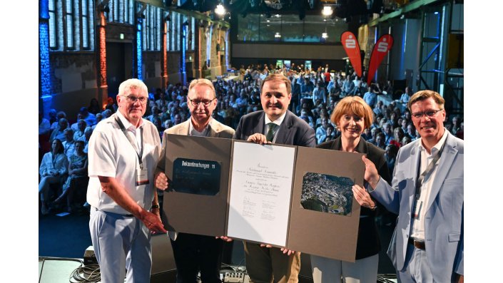 Sebastian Schuster, Jochen Hagt, Nathaniel Liminski, Henriette Reker unf Stephan Santelmann stehen gemeinsam uaf der Bühne und halten eine Urkunde hoch.