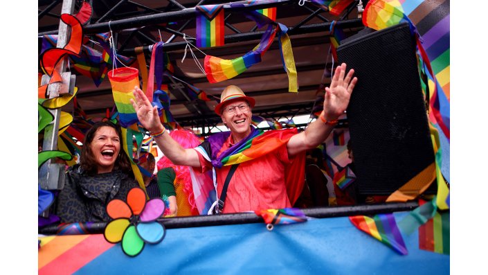 Eine buntkostümierte, feiernde Person auf dem CSD-Wagen der Hochschulen