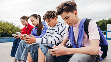 Vier Teenager schauen auf ihr Handy (Bild: Maria Vitkovska/AdobeStock)
