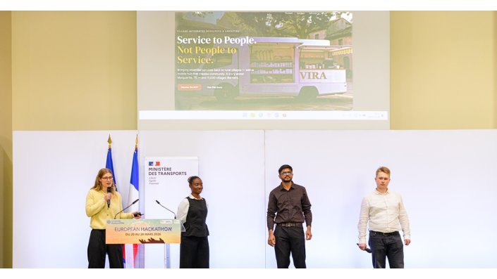 [Foto] Vier Personen auf einer Bühne bei einer Präsentation, zwei Frauen und zwei Männer, im Hintergrund eine Projektionsfläche mit der Überschrift „Service to People. Not People to Service.“ und einem Bild eines kleinen Lkws mit Waren.