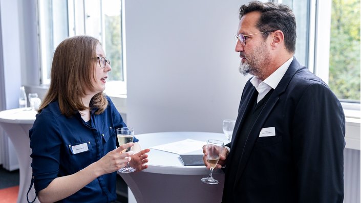 [Foto] Zwei Personen mit Sektgläsern in der Hand im Gespräch.
