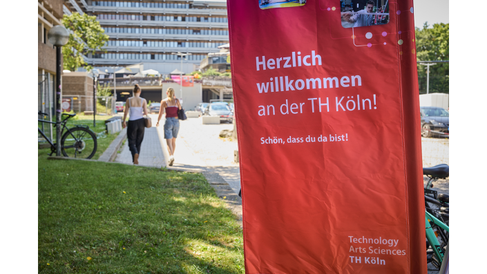 Studieninteressierte  auf dem Campus Deutz. Im Vordergrund steht ein Banner der TH Köln mit der Aufschrift: "Schön, dass Du da bist."