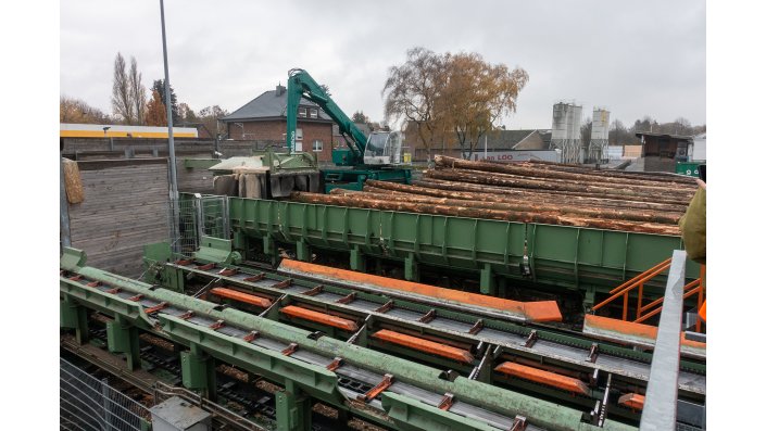 Im Bild ist ein kleiner Teil des Rundholzplatzes (im Hintergrund) und im Vordergrund die Anlage zur Anpassung des Wurzelstocks zu sehen. Noch weiter vorne fällt der Blick auf Förderanlagen, auf denen die Fichten- und Douglasienholzstämme in die Sägehalle transportiert werden.