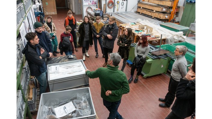 Markus Wittköpper (im Bild vorne, den Rücken zugewendet), der Leiter der Nassholzkonservierungswerkstatt am RGZM, diskutiert mit der Gruppe die Vor- und Nachteile verschiedener Verfahren. Das Bild gibt auch einen Eindruck von den räumlichen Anfordernissen und der Ausstattung der Werkstatt wieder.