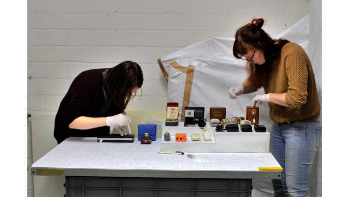 Zwei Studentinnen fertigen Umrisszeichnungen der Objekte auf den Regalböden an.