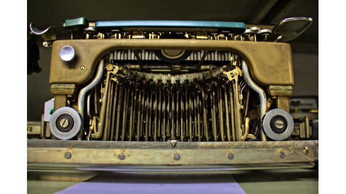 Eine alte Schreibmaschine von vorne aufgenommen. Die Ziffernhämmer erinnern vage an ein aufgerissenes Maul.