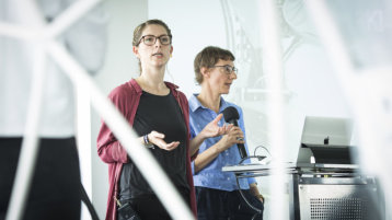 Zwei Frauen stehen vor einem Rednerpult und sprechen Zwei Frauen stehen vor einem Rednerpult und sprechen