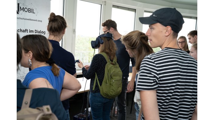 Mehrere Personen gucken einer Frau mit VR-Brille zu