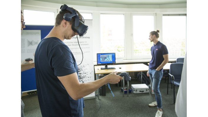 Ein Mann mit einer VR-Brille auf dem Kopf, ein anderer Mann im Hintergrund