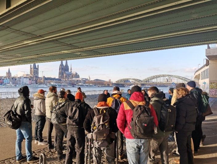 Eine Studierendengruppe unter der Deutzer Brücke mit Sicht auf den Dom und die Hohenzollernbrücke