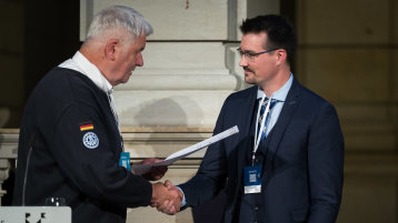 Albrecht Brömme übergibt die Urkunde zum dem Förderpreis des Deutschen Komitee für Katastrophenvorsorge e.V. an Chris Hetkämper (Bild: Laurin Schmid / bundesfoto)