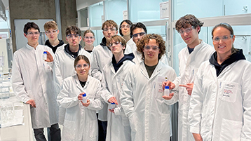 Der Chemie-Leistungskurs des Friedrich-Wilhelm-Gymnasiums steht mit Kitteln und Brillen im Labor. (Bild: TH Köln - Media Lab)
