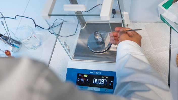 Zu sehen ist die Hand eines Teilnehmers vor einer Waage. Er wiegt 0,01 g des Coffeins mit einem stabartigen Messgerät ein.