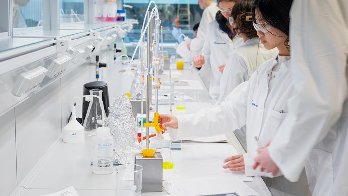 Die junge Nachwuchsforscher*innen stehen an der Werkbank im Labor und arbeiten mit gelöstem Fluorescein, um Chlorid zu bestimmen