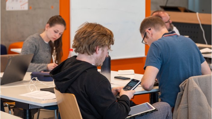 Studierenden sitzen an Tischen und arbeiten mit ihren Taschenrechnern.