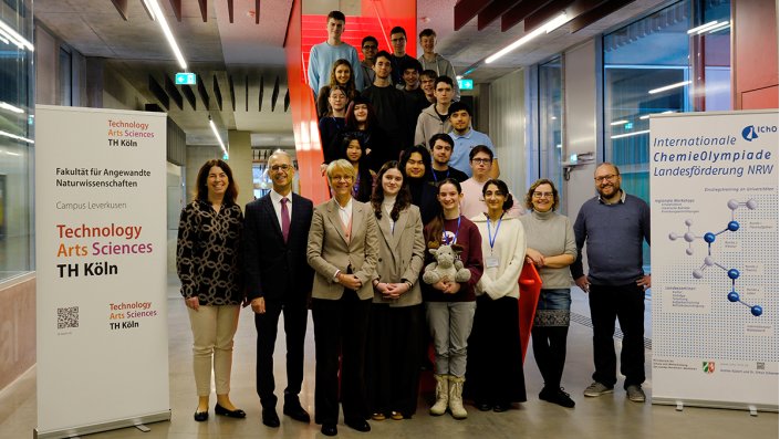 Auf der roten Treppe am Campus Leverkusen stehen 18 Schüler*innen mit Ministerin Dorothee Feller, Referentin Ines Op de Hipt, den Landesbeauftragten Andrea Küsters sowie Dr. Simon Scheren und Prof. Dr. Dirk Burdinski.
