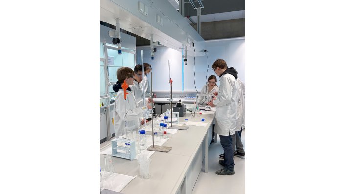 Die Schüler*innen stehen an der Werkbank vor führen an der Waage die Gehaltsbestimmung ihrer Produkte durch.