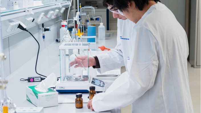 Zwei Schüler stehen vor einer Waage und wiegen eine Substanz.