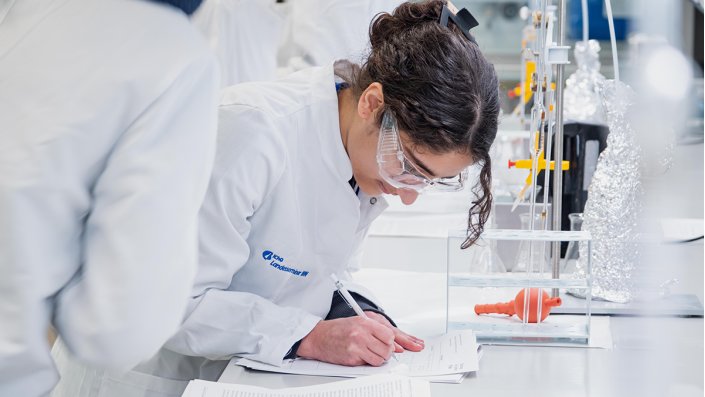 Eine Schülerin steht an der Werkbank und notiert die Beobachtungen und Ergebnisse im Laborjournal.