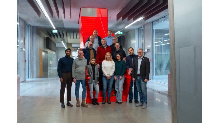 Die Projektpartner von Aquasan stehen im Flur des Campus Leverkusen vor der roten Treppe.
