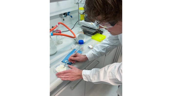 Ein Schüler zerkleinert vorsichtig sein Produkt auf einem Uhrglas, bevor es in den Trockenschrank kommt.