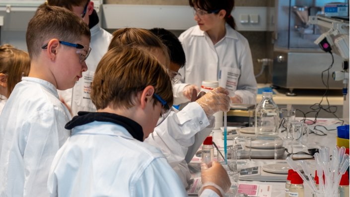 Die jungen Forscher*innen geben Natriumalginat-Lösung tropfenweise mit einer Pipette in flüssiges Calciumchlorid.