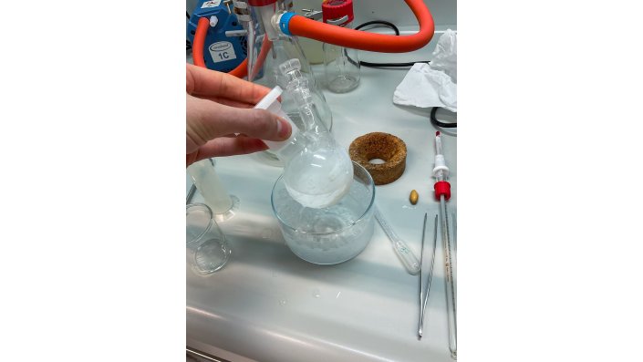 Ein Schüler holt einen Kolben mit Flüssigkeit aus einem weiteren Gefäß mit Flüssigkeit.