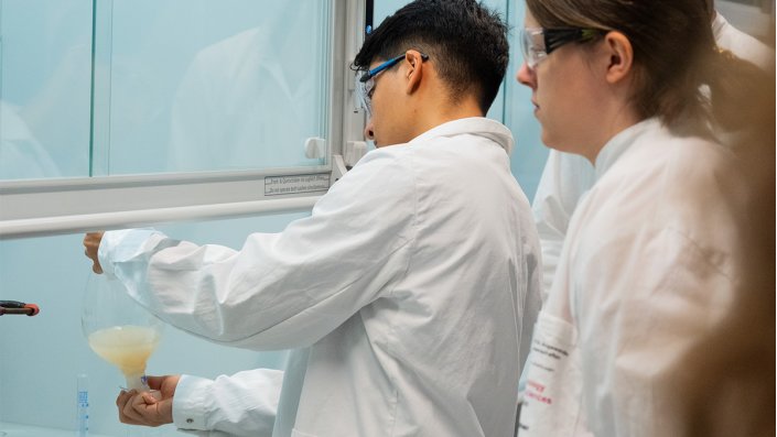 Ein Schüler extrahiert unter dem Abzug das Coffein aus der wässrigen Phase mit einem Schütteltrichter.