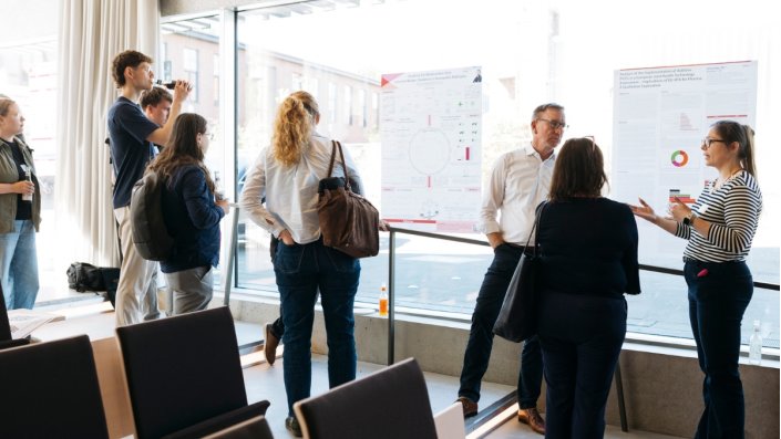 Zwei Promovierende der Fakultät für Angewandte Naturwissenschaften stehen vor ihren Postern und sind im Gespräch mit Gästen.