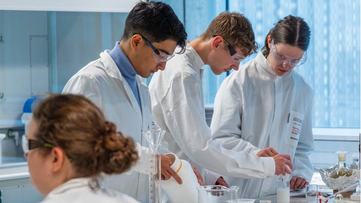 Drei Schüler*innen stehen im Labor und befüllen einen Behälter