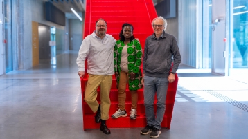  Prof. Dr. Séphan Barbe, Dr. Ossénatou Mamadou und Prof. Dr. Philipp Davies stehen nebeneinander vor der roten Treppe am Campus Leverkusen (Bild: TH Köln - Media Lab)