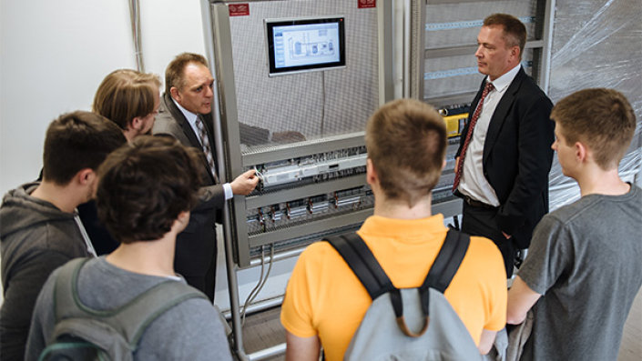 Wolfgang Lütkeniehoff, Leiter der Siemens-Businessunit Building Technologies und Prof. Dr. Jochen Müller, Leiter des Labors für Gebäudeautomation und Regelungstechnik mit Studierenden vor den von Siemens gespendeten Komponenten