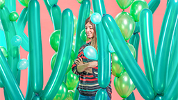 Eine Frau steht vor einem rosa Hintergrund zwischen grünen Luftballons, die wie Kakteen arrangiert sind. (Bild: Sarah Illenberger)